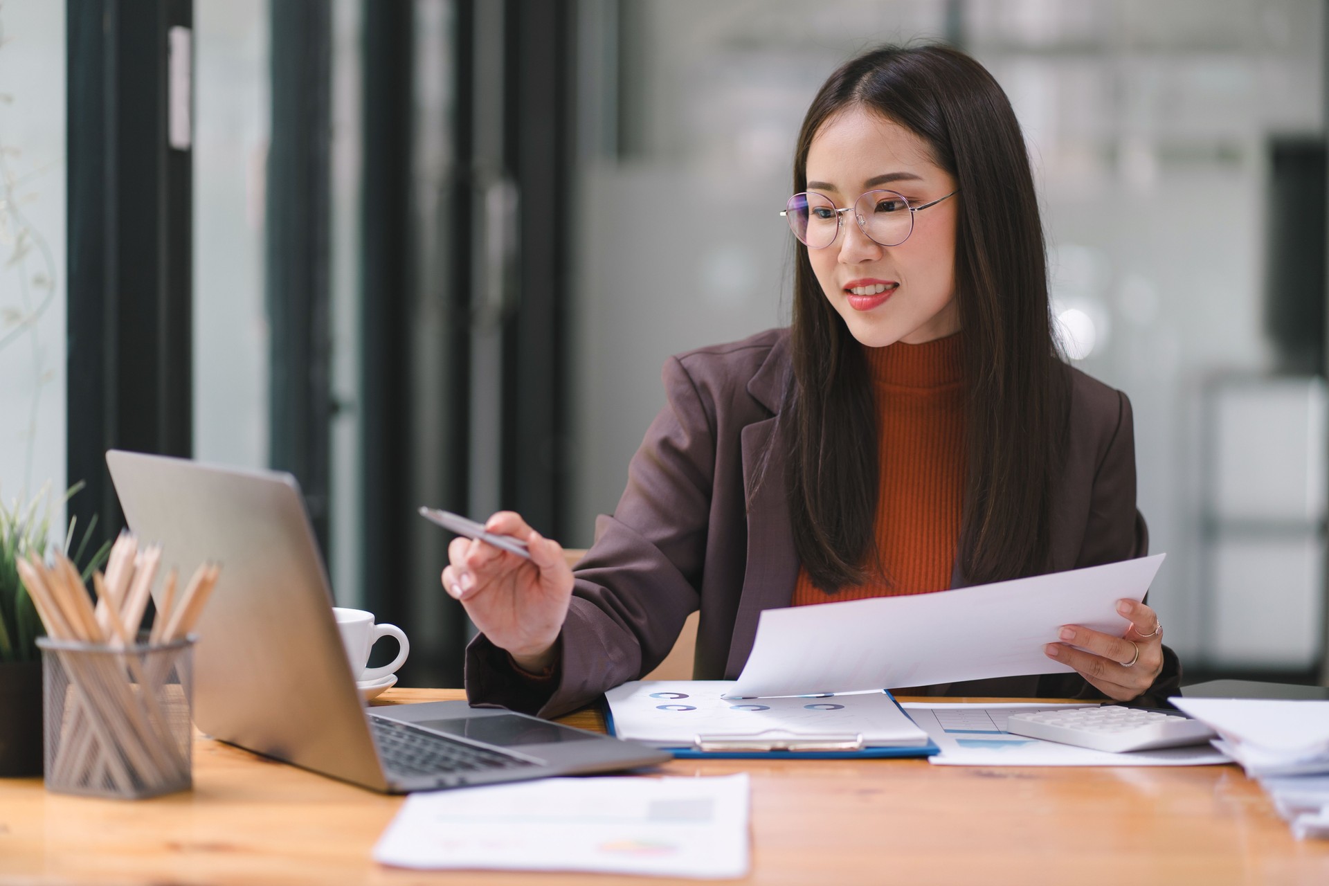 Asian businesswoman or accountant using a calculator, graphs, and charts to analyze market data, balance sheets, accounts, and net profits.